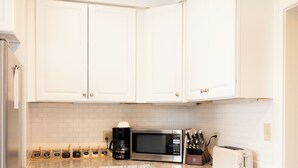 Une cuisine avec des meubles blancs, un four à micro-ondes, un grille-pain et une machine à café.