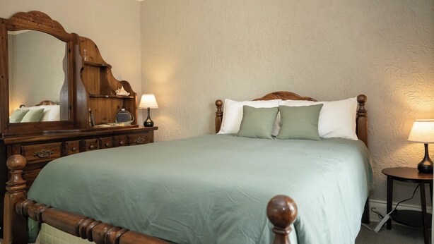 Un lit bien fait, avec une tête de lit en bois, une table de chevet avec une lampe et un grand miroir.