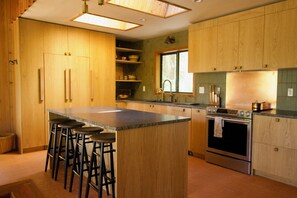 Eine Küche mit Holzausstattung, einer zentralen Kochinsel mit Barhocker, einem Edelstahlbackofen und einem Fenster.