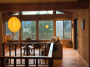 Ein Holzblock-Interieur mit einem großen Fenster, einem hängenden Laternenlicht, einem Sofa und einem Esstisch.