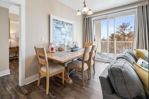 Un comedor con mesa y sillas de madera, un cuadro en la pared y un balcón con cortinas.