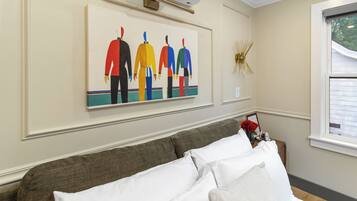 A room with a bed, a wall-mounted air conditioner, a framed artwork, and a window with blinds.