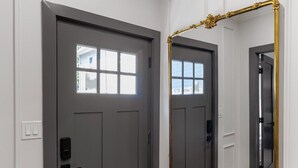 A hallway with a gray door, a large mirror with a gold frame, and a wooden floor.
