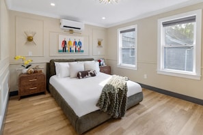 A bedroom with a large bed, a nightstand, a dresser, and a window.