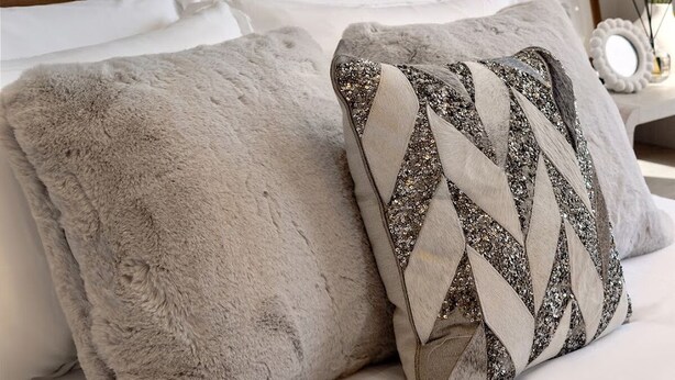 A bed with a wooden headboard, two pillows, a nightstand with a lamp, and a wall with a floral pattern.