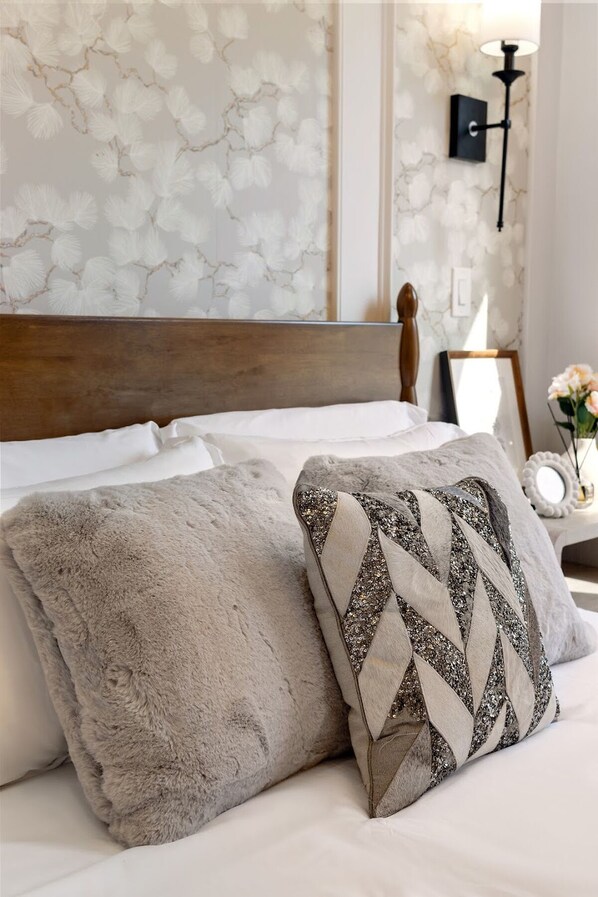 A bed with a wooden headboard, two pillows, a nightstand with a lamp, and a wall with a floral pattern.
