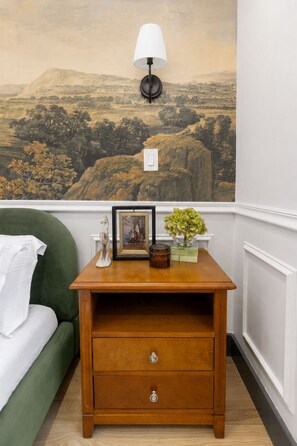 A room with a green sofa, a wooden nightstand with drawers, a lamp, and a landscape mural on the wall. - Cambridge Designer Home / Harvard, MIT, Boston (Cambridge)