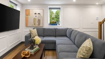 A modern living room with a sectional sofa, a flat-screen TV, and a coffee table with books and decorative items.