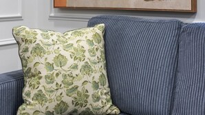 A painting of two figures on a wall, a cushion on a couch, and a framed artwork.