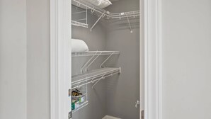 A narrow walk-in closet with white metal shelving units, some with folded white towels. - Spacious family home sunrise and sunset views, close to beach and resort amenities (Saint Helena)
