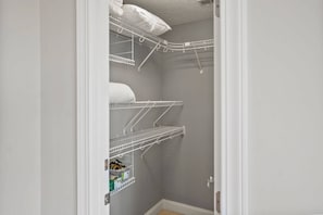 Ein schmaler begehbarer Kleiderschrank mit weißen Metallregalen, einige mit gefalteten weißen Handtüchern.