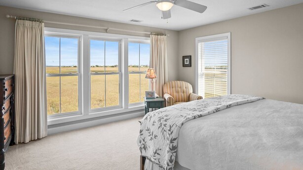 A bedroom with a large bed, a ceiling fan, a chair, a nightstand, and a window with a view of a field. - Spacious family home sunrise and sunset views, close to beach and resort amenities (Saint Helena)