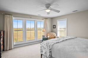Ein Schlafzimmer mit einem großen Bett, einem Deckenventilator, einem Sessel, einem Nachttisch und einem Fenster mit Blick auf ein Feld.