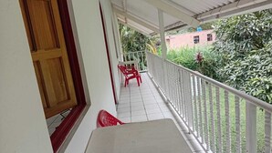 Ein Balkon mit weißer Brüstung, einem roten Kunststoffstuhl und einem Tisch.
