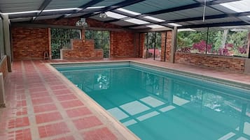 An indoor swimming pool with a tiled floor, brick walls, and a glass ceiling.