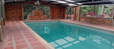 An indoor swimming pool with a tiled floor, brick walls, and a glass ceiling.