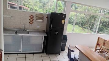 A kitchen with a sink, a refrigerator, a window with a view of greenery, and a wooden bench.