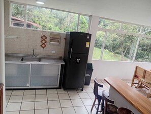 A kitchen with a sink, a refrigerator, a window with a view of greenery, and a wooden bench.