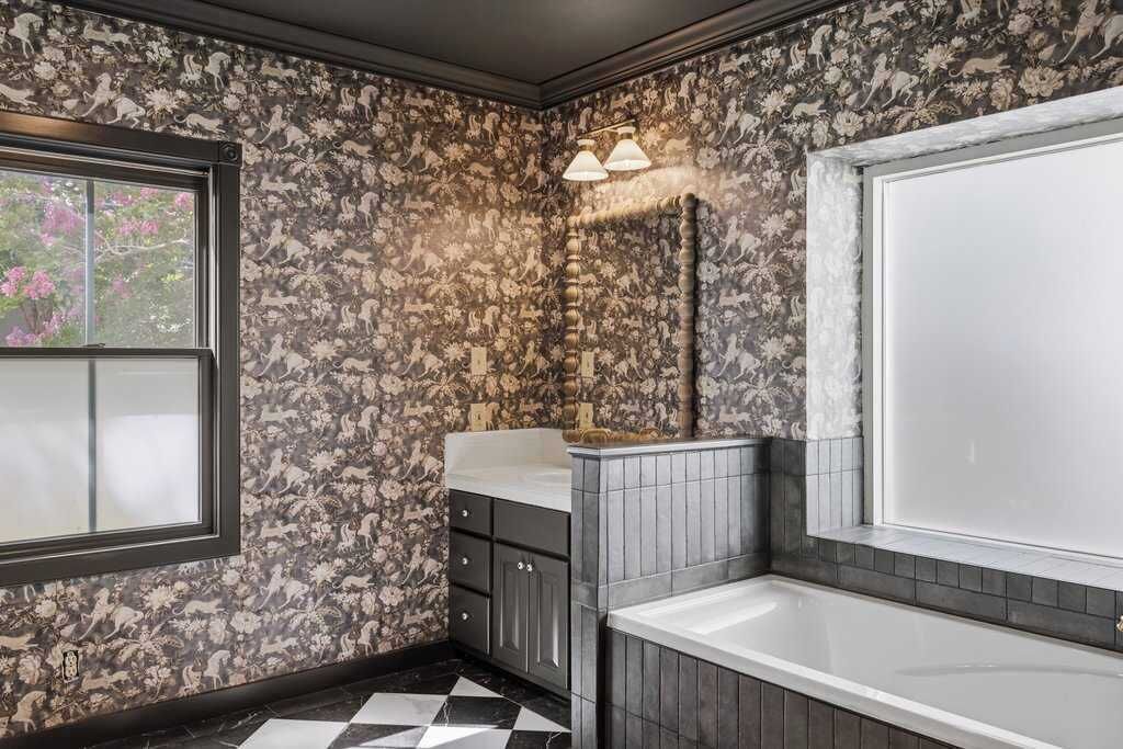 A bathroom with a patterned wallpaper, a bathtub, a sink, and a window.
