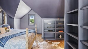 A bedroom with a sloped ceiling, a bed with a patterned bedspread, a bookshelf, and a cowhide rug. - Painted Lady - Pool, Hot Tub & Walk to Main (Fredericksburg)