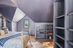 A bedroom with a sloped ceiling, a bed with a patterned bedspread, a bookshelf, and a cowhide rug. - Painted Lady - Pool, Hot Tub & Walk to Main (Fredericksburg)