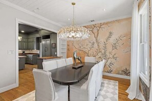 A dining area with a large table, white chairs, and a chandelier. - Painted Lady - Pool, Hot Tub & Walk to Main (Fredericksburg)