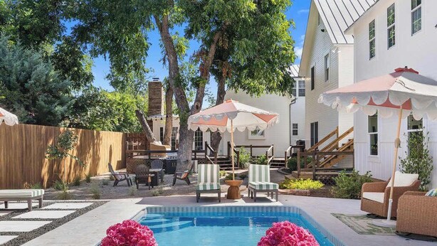 A swimming pool with two flower arrangements, outdoor furniture, and a wooden fence. - Painted Lady - Pool, Hot Tub & Walk to Main (Fredericksburg)