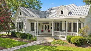 A white house with a porch, a covered entryway, and a well-maintained lawn. - Painted Lady - Pool, Hot Tub & Walk to Main (Fredericksburg)