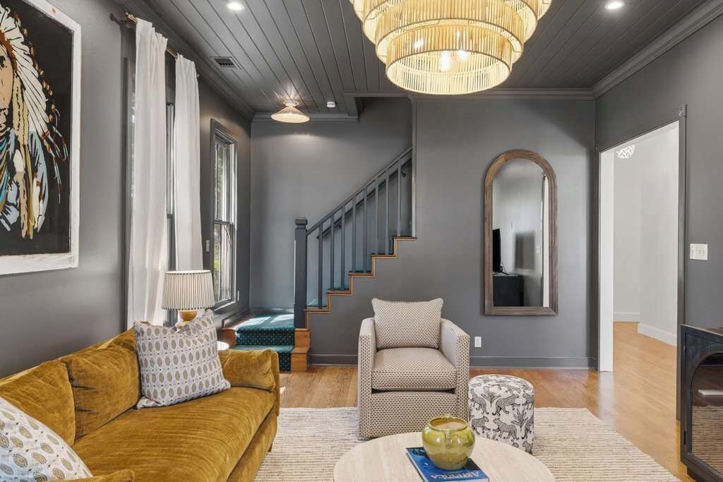 A living room with a sofa, armchair, and ottoman, a staircase, and a large mirror.