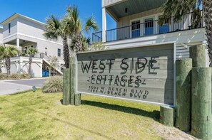 Skilt for 'West Side Cottages' med udsigt til bygningen og omkringliggende palmer.