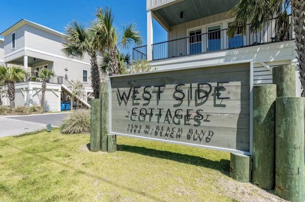 Bordje voor 'West Side Cottages' met uitzicht op het gebouw en omliggende palmbomen.