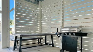 Ein Außenbereich mit Terrasse, Grillstation und Sitzbank.
