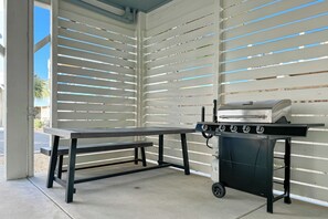 Ein Außenbereich mit Terrasse, Grillstation und Sitzbank.