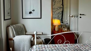 Ein Zimmer mit einem Bett, einem Sessel, einer Lampe, einem Schminktisch und einer Tür.