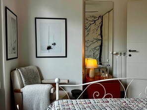 A room with a bed, a chair, a lamp, a dresser, and a door. - Vista Lago 99 is a newly renovated apartment (Plesio)