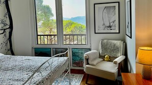 Ein Schlafzimmer mit einem Bett, einem Sessel, einem Fenster mit Aussicht und einer Lampe.