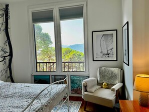 A bedroom with a bed, a chair, a window with a view, and a lamp. - Vista Lago 99 is a newly renovated apartment (Plesio)