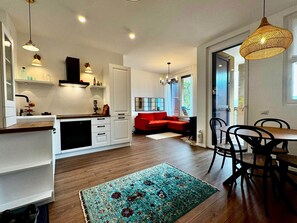 A modern kitchen with white cabinets, a red sofa, and a dining area with a table and chairs. - Vista Lago 99 is a newly renovated apartment (Plesio)