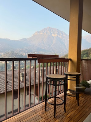 A balcony with wooden flooring, two wicker chairs, and a view of a mountain. - Vista Lago 99 is a newly renovated apartment (Plesio)
