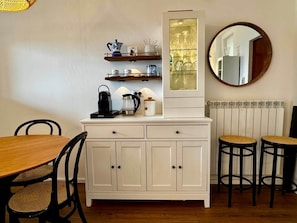 A dining area with a wooden table and chairs, a white cabinet with drawers, a coffee maker, and a mirror on the wall. - Vista Lago 99 is a newly renovated apartment (Plesio)