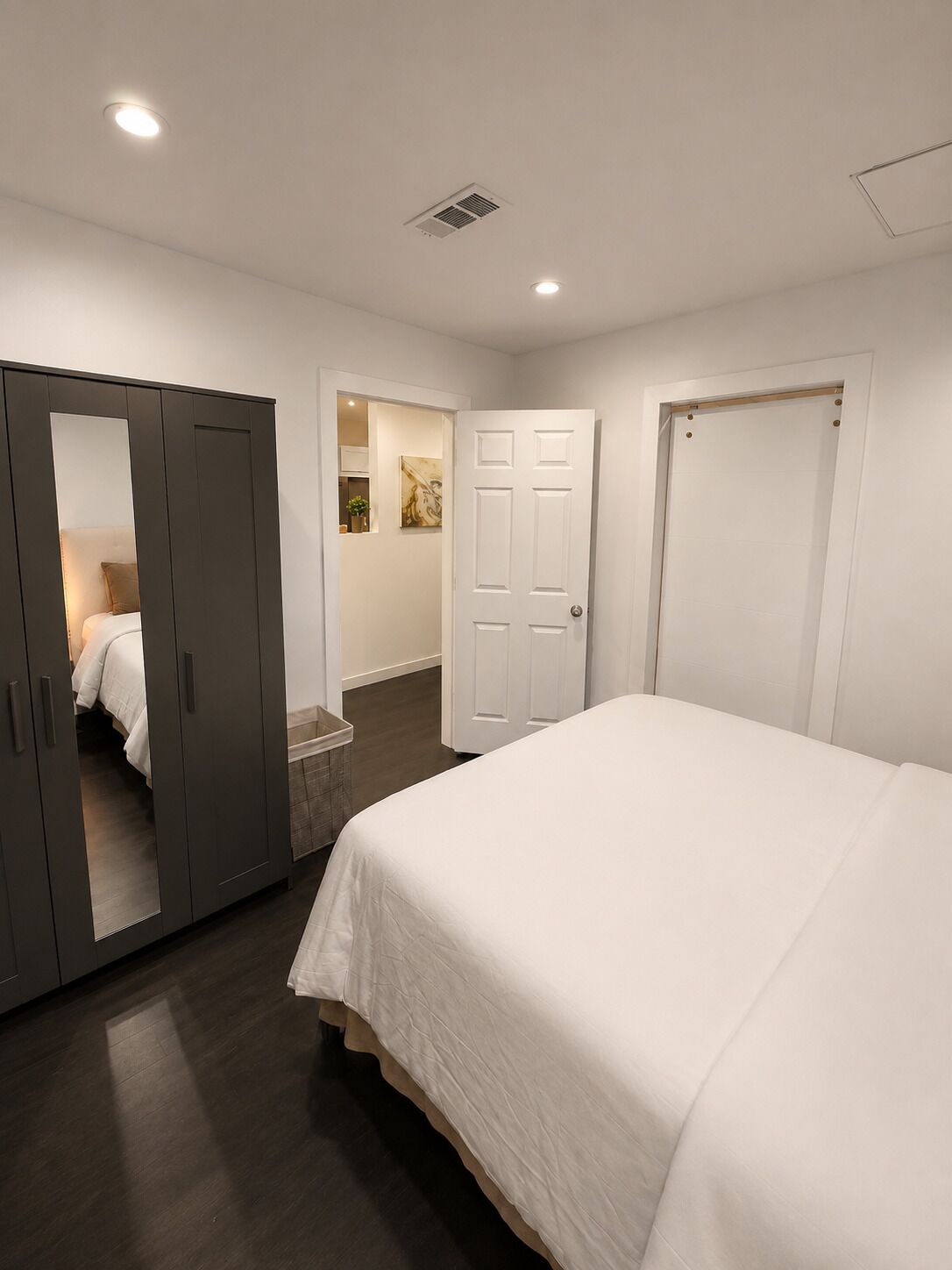 A bedroom with a large bed, a wardrobe, and a door leading to another room.