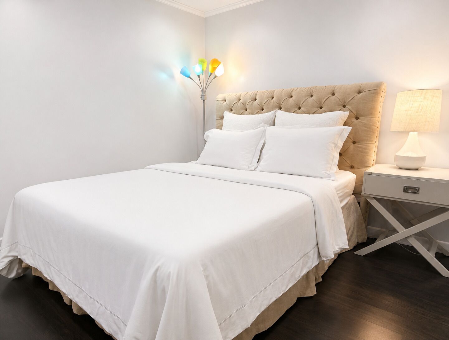 A neatly made bed with a tufted headboard, a bedside table with a lamp, and a wall-mounted light fixture.