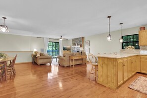 Un vaste espace de vie comprenant un coin repas avec une table en bois, un canapé et une cuisine dotée d’un grand îlot central.
