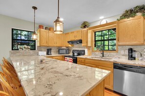A kitchen with wooden cabinets, a marble countertop, a stainless steel dishwasher, and a large window. - Sasquatch Beech 3BR Beech Mountain Home- Near Skiing- Fire pit- Sleeps 8 (Beech Mountain)