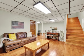 A living room with a wooden coffee table, a brown leather sofa, a wooden staircase, and a wall-mounted American flag. - Sasquatch Beech 3BR Beech Mountain Home- Near Skiing- Fire pit- Sleeps 8 (Beech Mountain)