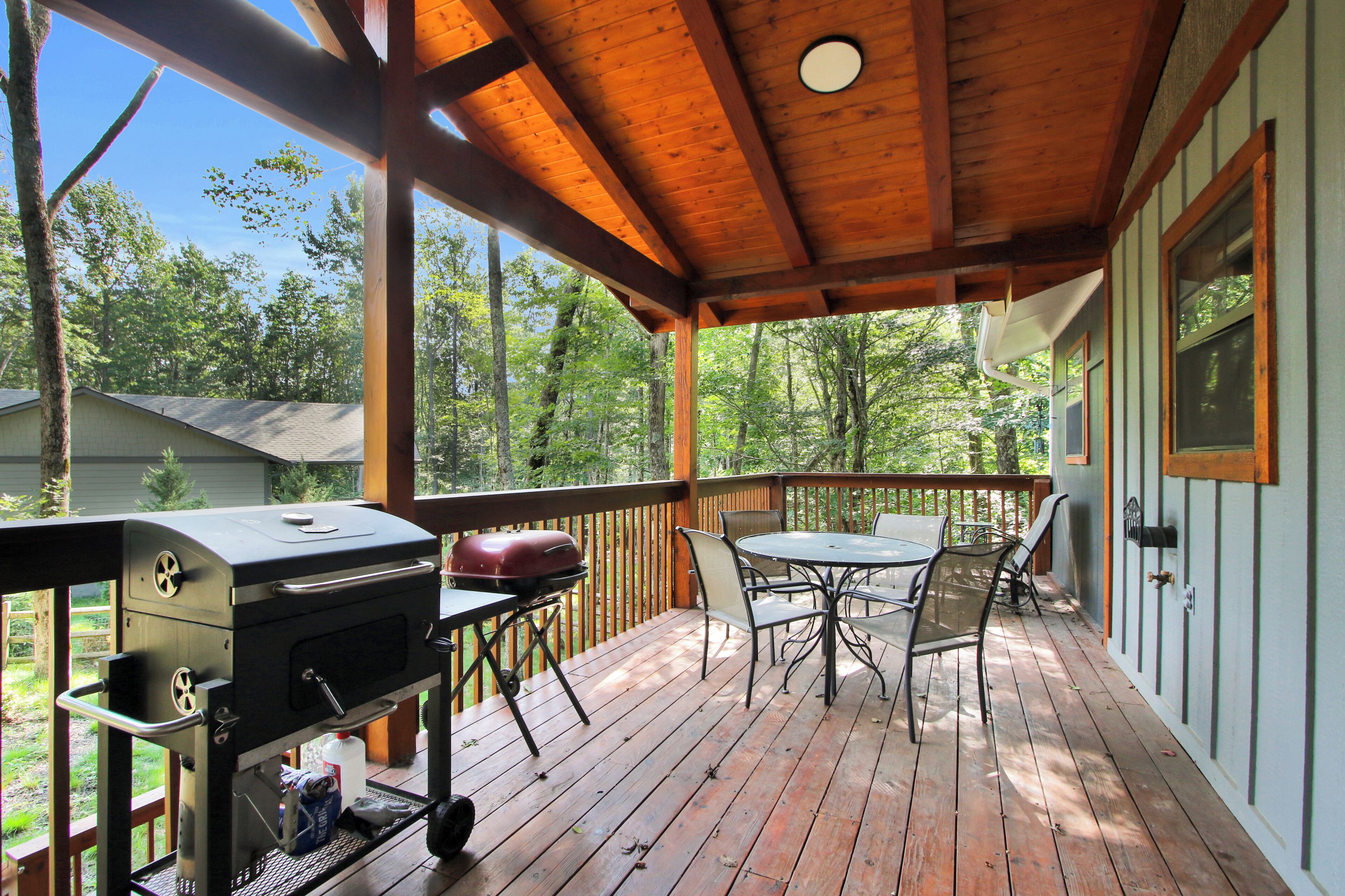A covered outdoor deck with a grill, table, and chairs.