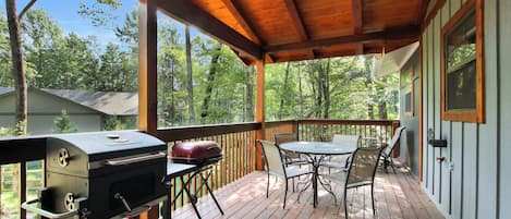 A covered outdoor deck with a grill, table, and chairs.