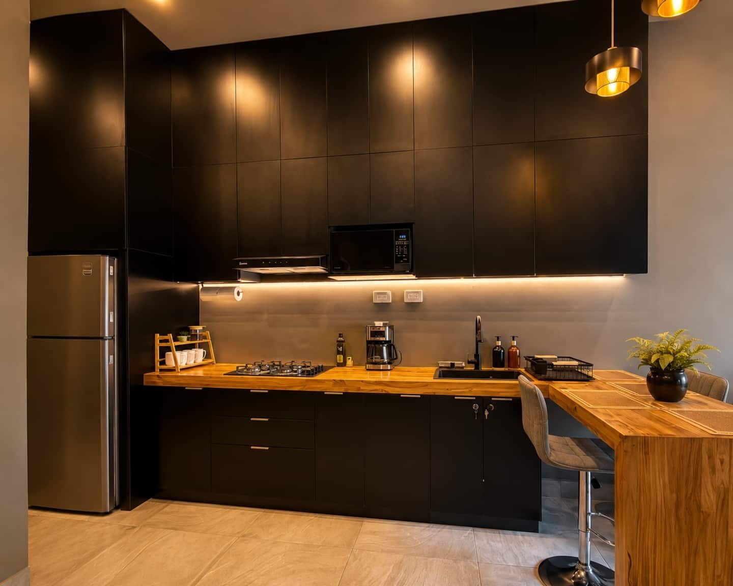 A modern kitchen with dark cabinetry, a stainless steel refrigerator, a microwave, and a wooden countertop.