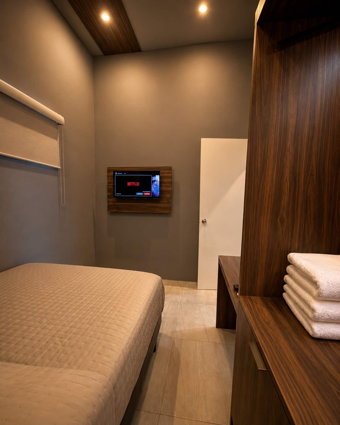 Une chambre à coucher moderne avec un lit, une armoire en bois, un téléviseur fixé au mur et une porte.