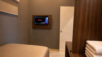 Une chambre à coucher moderne avec un lit, une armoire en bois, un téléviseur fixé au mur et une porte.